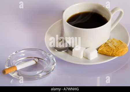 A cup of coffee with a burning cigarette in an ash tray Stock Photo