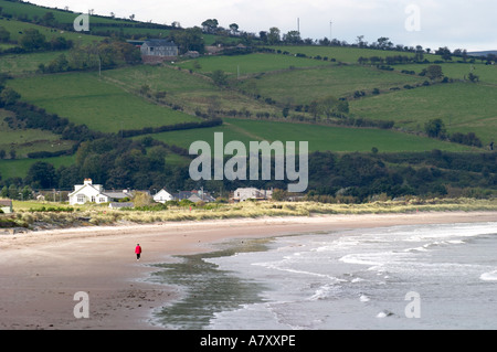 woman in red coat walks alone along the sandy beach waterfoot glenarrif county Antrim Northern Ireland Stock Photo