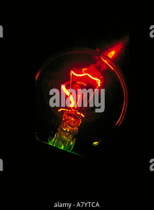 Close up details showing incandescent light bulb and filament in the dark emitting light and heat when electric current is passed through it. Stock Photo