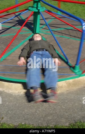 Young boy playing on playground roundabout in a childrens playground Stock Photo