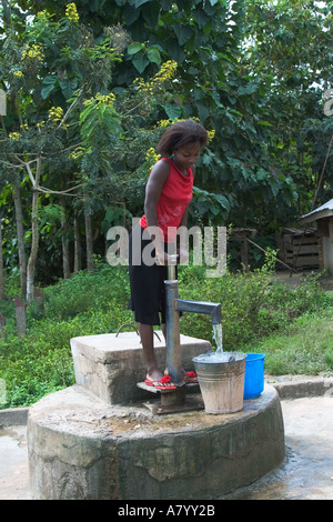 Young woman using hand pump for pumping potable and safe drinking water from borehole in the village centre Ghana West Africa Stock Photo