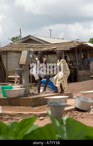 Young boy and girl using hand pump for pumping potable and safe drinking water from borehole in the village centre Ghana West Africa Stock Photo