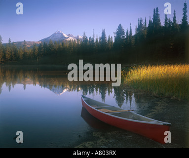 Red canoe beached on the shore of Sparks Lake with early morning light filtering across the landscape Stock Photo