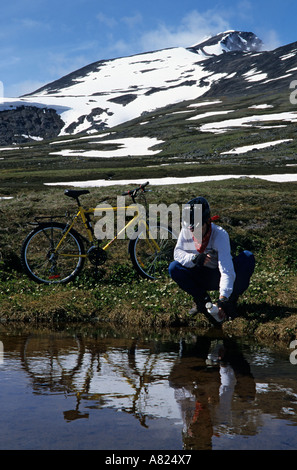 Mountain biker getting drink from alpine lake Hudson Bay Mountain Smithers British Columbia Stock Photo