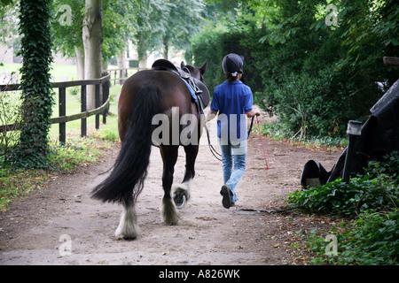A young girl leads her horse back to stables along a woodland path after a ride, Chippenham, Cambridgeshire, UK Stock Photo