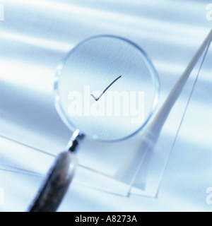 Magnifying glass over blank papers highlighting a check mark blue tone Stock Photo