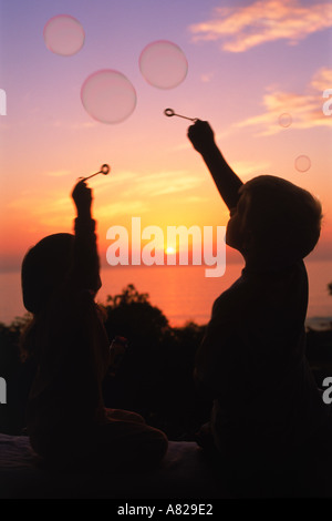 Two children reaching for airborne bubbles at sunset Stock Photo