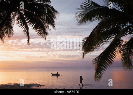One women walking and one paddling outrigger canoe on Aitutaki Island in Cook Islands