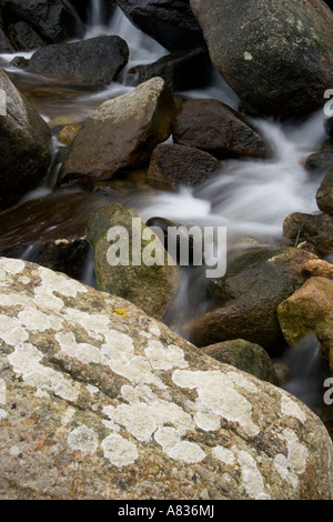 Water flowing between rocks with a lichen covered boulder in the foreground. Stock Photo