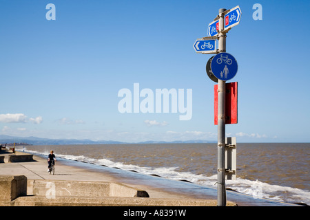 Signpost for Cycle Route 5 with cyclist on seafront promenade track by beach at high tide Prestatyn Denbighshire North Wales UK Stock Photo
