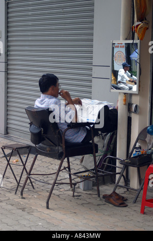 Barber reading the newspaper on the street Saigon Vietnam Stock Photo