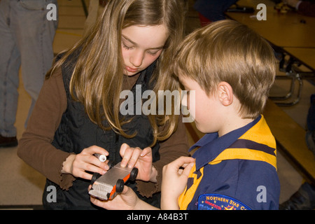 Sister helping Cub Scout lubricate race car Pinewood Derby age 14 and 7. Horace Mann Elementary School 'St Paul' Minnesota USA Stock Photo