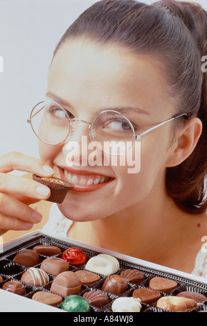 Studio portrait of woman about to eat a chocolate from a selection box. Stock Photo