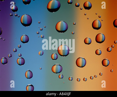 Still life close-up of water droplets on glass surface against backdrop of spectral colours. Stock Photo