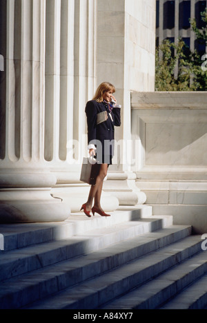 Young woman with cellphone standing on steps of official building. Stock Photo