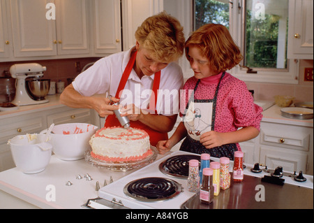 Family. Mother and daughter indoors in kitchen icing a cake. Stock Photo