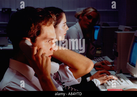Call centre telephone operators with computer monitor screens at night. Stock Photo