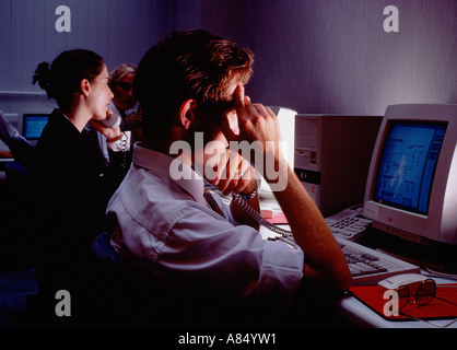 Call centre telephone operators with computer monitor screens at night. Stock Photo