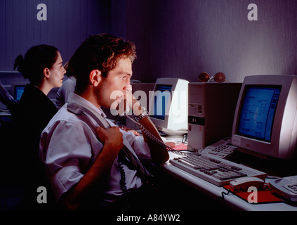 Call center telephone operators. Man using telephone whilst referring to computer screen.  Woman in background. Stock Photo