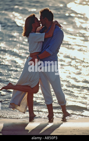 Young romantic couple standing on a beach at water's edge. Stock Photo