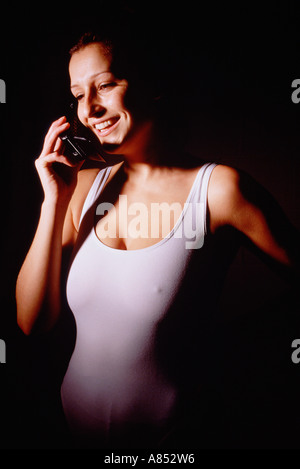 Indoor portrait of young woman in exercise leotard using a mobile 'phone. Stock Photo