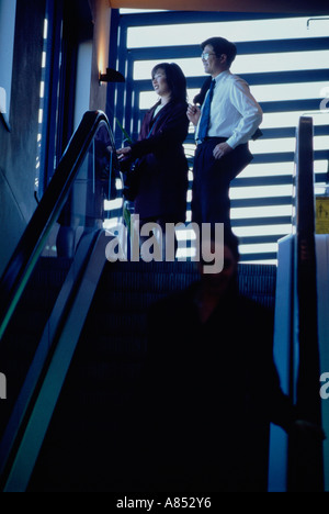 Two office workers in building standing by escalators. Stock Photo