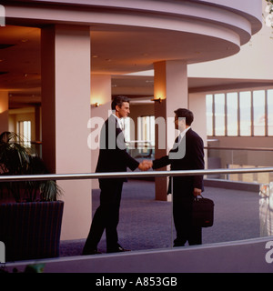 Two businessmen shaking hands on mezzanine interior of modern office building. Stock Photo