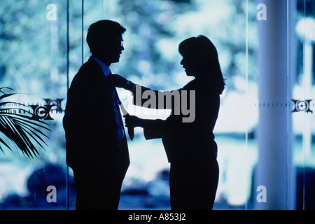 Interior close-up side view silhouette of woman adjusting businessman's tie. Stock Photo