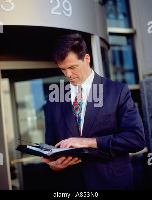 Business Professional. Executive man outside city office building. Looking in diary. Stock Photo