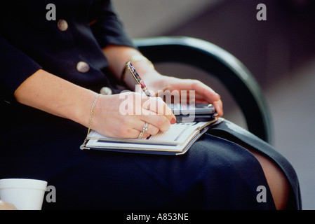 Close-up of young woman's lap hand writing in diary Stock Photo