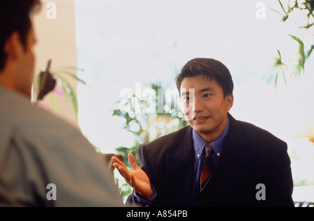 Close-up of Chinese business executive man talking with a European man on restaurant  terrace. Stock Photo