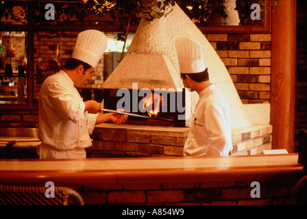 Two men hotel chefs in whites tending pizza oven in restaurant. Stock Photo