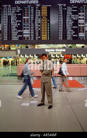 Busy Singapore airport terminal with young man using mobile 'phone. Stock Photo