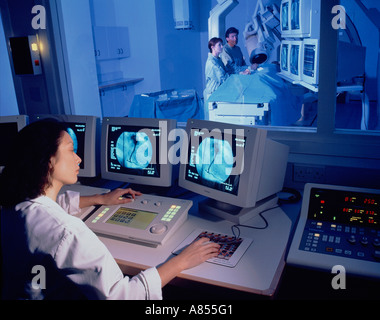 Nurse in computerized control room overlooking surgeon and nurse with patient in hospital Angiography scanning room. Stock Photo