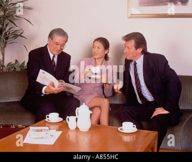Two men and a woman informal meeting in an office seated at coffee table. Stock Photo