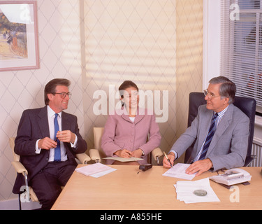Two men and a woman meeting in an office seated at desk. Stock Photo