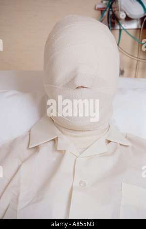 Close-up head and shoulders portrait of male patient in hospital bed with serious burns bandages covering his face. Stock Photo