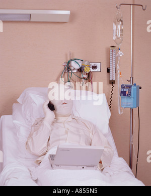 Close-up of male patient in hospital bed with serious burns bandages covering his face and arms using mobile 'phone. Stock Photo