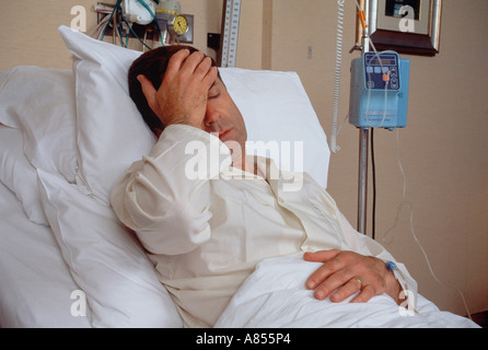 Middle age man in hospital bed with hand on forehead. Stock Photo