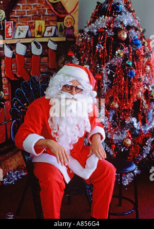 Santa Claus (Father Christmas) sitting in store setting by Christmas tree Stock Photo