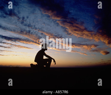 Central Australia. Simpson Desert. Sunset. Silhouette of young man crouching. Stock Photo