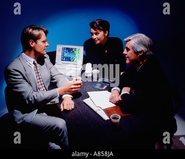 Two men and a woman in suits at late night business meeting with laptop. Stock Photo