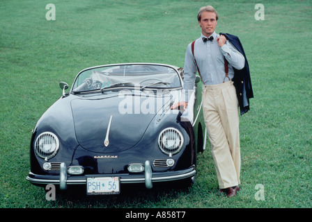 Stylish young man standing outdoors beside classic vintage Porsche sports car. Stock Photo