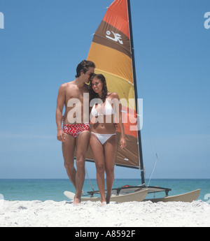 Healthy young couple walking on beach near small sailboat Stock Photo