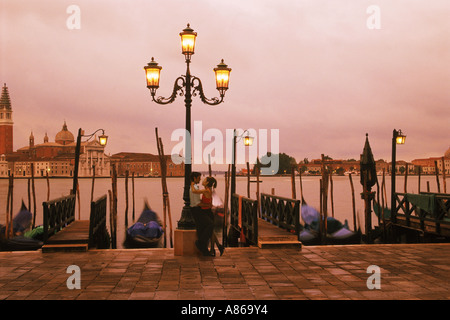 Couple embracing against lamp post on waterside walkway near St Marks Square in Venice, Italy Stock Photo