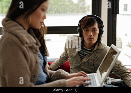 Young man hearing music while woman using laptop, side view Stock Photo