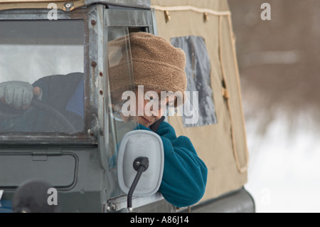 Mid aged woman wearing a woolen hat driving a 1965 Series 2a Land Rover SWB soft top diesel on snowy winter journey. Stock Photo