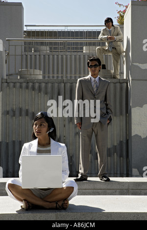 A woman works on a laptop while her colleagues are in the background. Stock Photo