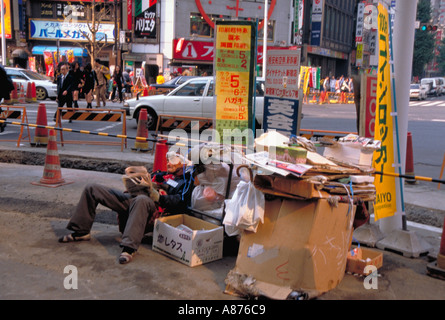 JAPAN Honshu Tokyo Homeless man living on the street with his cardboard home on sidewalk pavement at a busy road junction Stock Photo