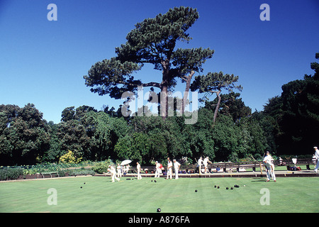 A group of people wearing white hats playing croquet on the lawn Trees and blue sky are in the background Stock Photo